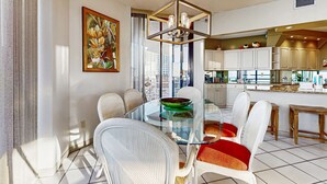 A modern kitchen with white cabinets, a glass dining table, and a city view. - Spacious waterfront condo w/ shared pool/hot tub/gym & beach access (Miramar Beach)