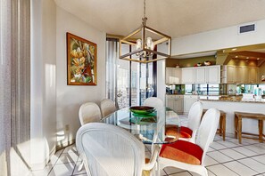 A modern kitchen with white cabinets, a glass dining table, and a city view. - Spacious waterfront condo w/ shared pool/hot tub/gym & beach access (Miramar Beach)