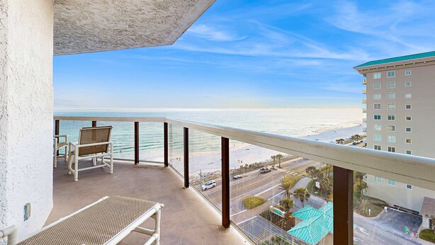 A balcony with a view of the beach and ocean. There are two wicker chairs and a table. - Spacious waterfront condo w/ shared pool/hot tub/gym & beach access (Miramar Beach)