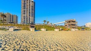 A sandy beach with a high-rise building and a wooden structure with a staircase. - Spacious waterfront condo w/ shared pool/hot tub/gym & beach access (Miramar Beach)