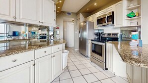 A modern kitchen with white cabinets, stainless steel appliances, and a granite countertop. - Spacious waterfront condo w/ shared pool/hot tub/gym & beach access (Miramar Beach)