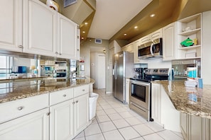 A modern kitchen with white cabinets, stainless steel appliances, and a granite countertop. - Spacious waterfront condo w/ shared pool/hot tub/gym & beach access (Miramar Beach)
