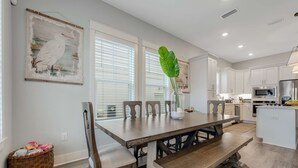 Una cocina moderna con armarios blancos, una mesa de comedor de madera con bancos y un ventanal con persianas.