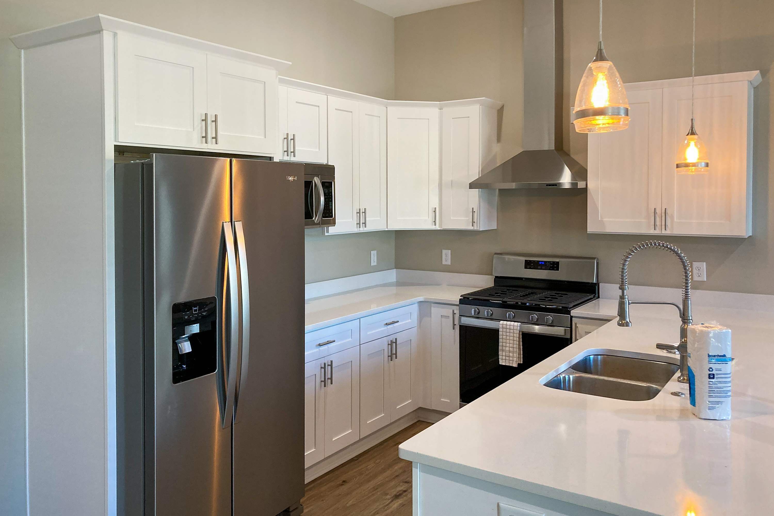 A modern kitchen with white cabinets, stainless steel appliances, and pendant lighting.