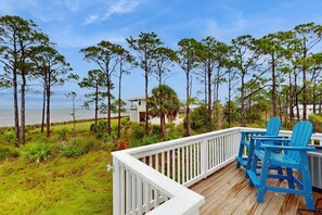 A wooden deck with blue Adirondack chairs overlooking a beach with tall pine trees and a white building in the background. - Gorgeous coastal home with plenty of space and easy beach access (St. George Island)