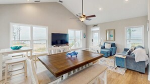 A spacious living area with a wooden dining table, white chairs, a blue sofa, and a television. - Gorgeous coastal home with plenty of space and easy beach access (St. George Island)