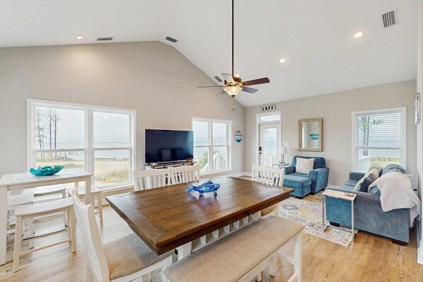 A spacious living area with a wooden dining table, white chairs, a blue sofa, and a television. - Gorgeous coastal home with plenty of space and easy beach access (St. George Island)