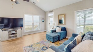 A spacious living room with a large flat-screen TV, a ceiling fan, and a view of the outdoors. - Gorgeous coastal home with plenty of space and easy beach access (St. George Island)