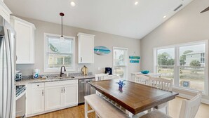 A modern kitchen with white cabinets, a wooden dining table, and a view of the outdoors. - Gorgeous coastal home with plenty of space and easy beach access (St. George Island)