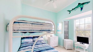 Ein Etagenbett mit gestreifter blau-weißer Bettwäsche, eine weiße Kommode, ein Fernseher auf einem kleinen Tisch und eine Haifisch-Dekoration an der Wand.