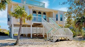 Ein zweistöckiges Strandhaus mit überdachter Veranda und einer Treppe, die zum oberen Stock führt.