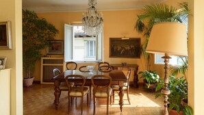 Uma sala de jantar com mesa e cadeiras de madeira, um candelabro e plantas em vasos.