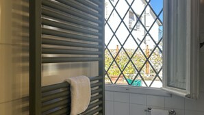 Um banheiro com porta-toalhas, uma janela com vista para edifícios e parede revestida de azulejos.