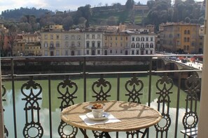 A balcony with a wicker table, a railing, and a view of a river with buildings in the background. - Starway to Heaven Apartment (Firenze)