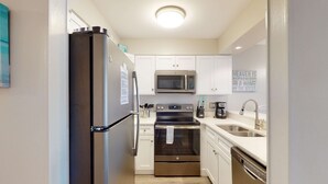 A compact kitchen with a refrigerator, oven, microwave, and dishwasher. - Updated ground-floor condo with patio, W/D, pool, BBQ area, & AC - near beach (Miramar Beach)