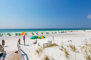A beach with white sand, green umbrellas, and a wooden walkway leading to beach chairs. - Waterfront corner condo w/ shared pool, pool spa, fitness room, & beach service (Miramar Beach)