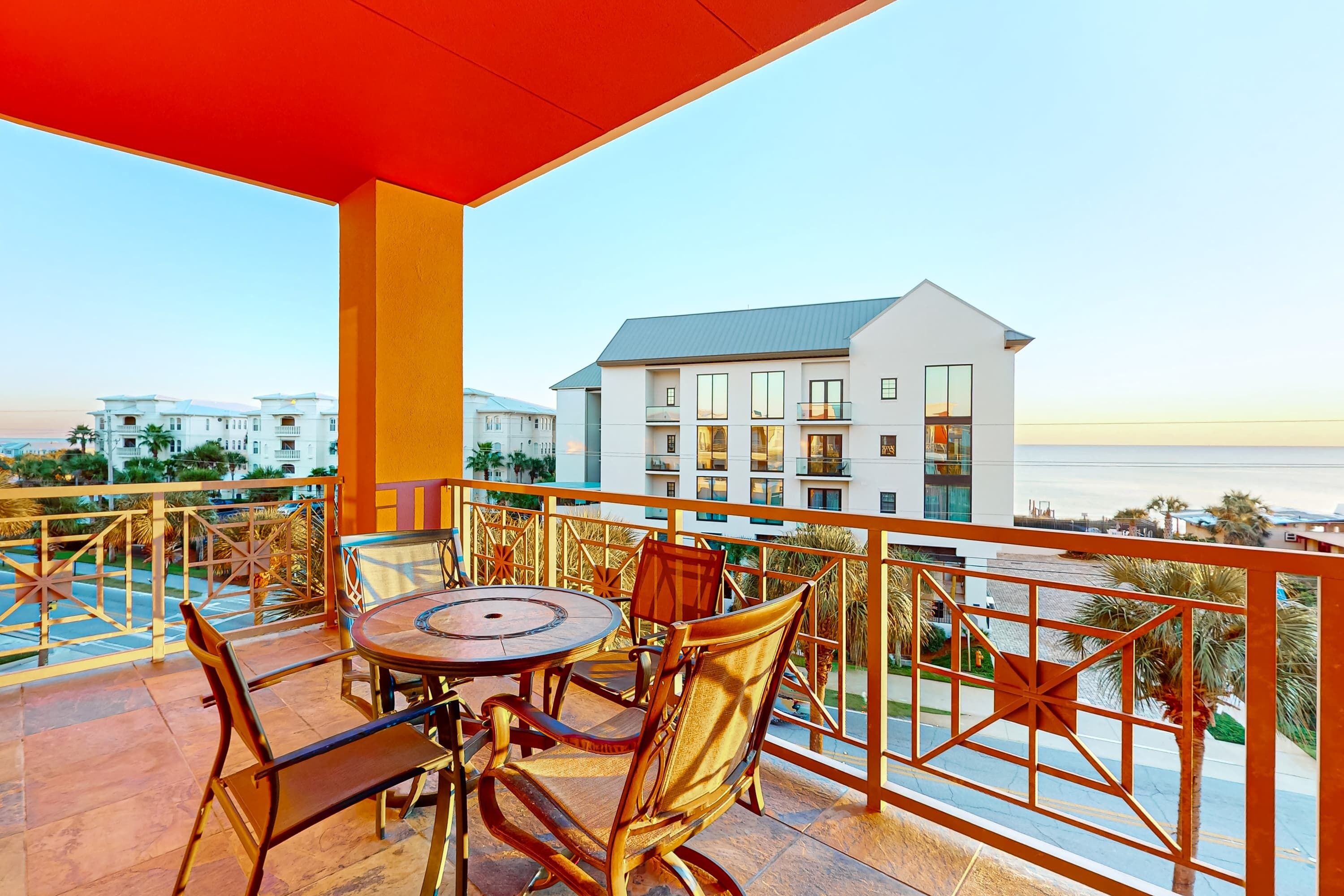 A balcony with a round table and chairs, overlooking a building and a body of water.