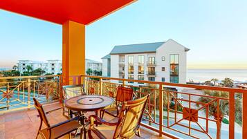 A balcony with a round table and chairs, overlooking a building and a body of water.