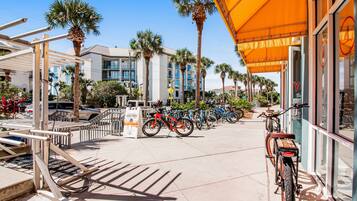 A sunny street with bicycles parked along the sidewalk, palm trees, and a building with a yellow awning.