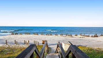 A wooden boardwalk leading to a beach with rows of sun loungers and a sandy shore.
