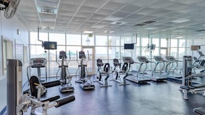 Ein Fitnessstudio mit verschiedenen Trainingsgeräten, großen Fenstern und Blick ins Freie.
