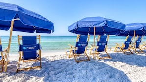 Strandstühle und Sonnenschirme sind auf einem Sandstrand aufgestellt, mit freiem Blick auf das Meer.