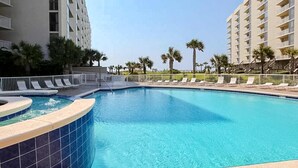 A swimming pool with a curved edge, surrounded by lounge chairs and palm trees. - 1st floor comfortable Gulf view condo, beach setup included, near dining (Miramar Beach)