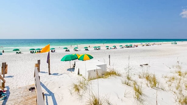 A beach with white sand, green and yellow umbrellas, and a wooden walkway leading to a white building. - 1st floor comfortable Gulf view condo, beach setup included, near dining (Miramar Beach)