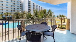 A balcony with a round table and four chairs, overlooking a swimming pool and a building with multiple balconies. - 1st floor comfortable Gulf view condo, beach setup included, near dining (Miramar Beach)