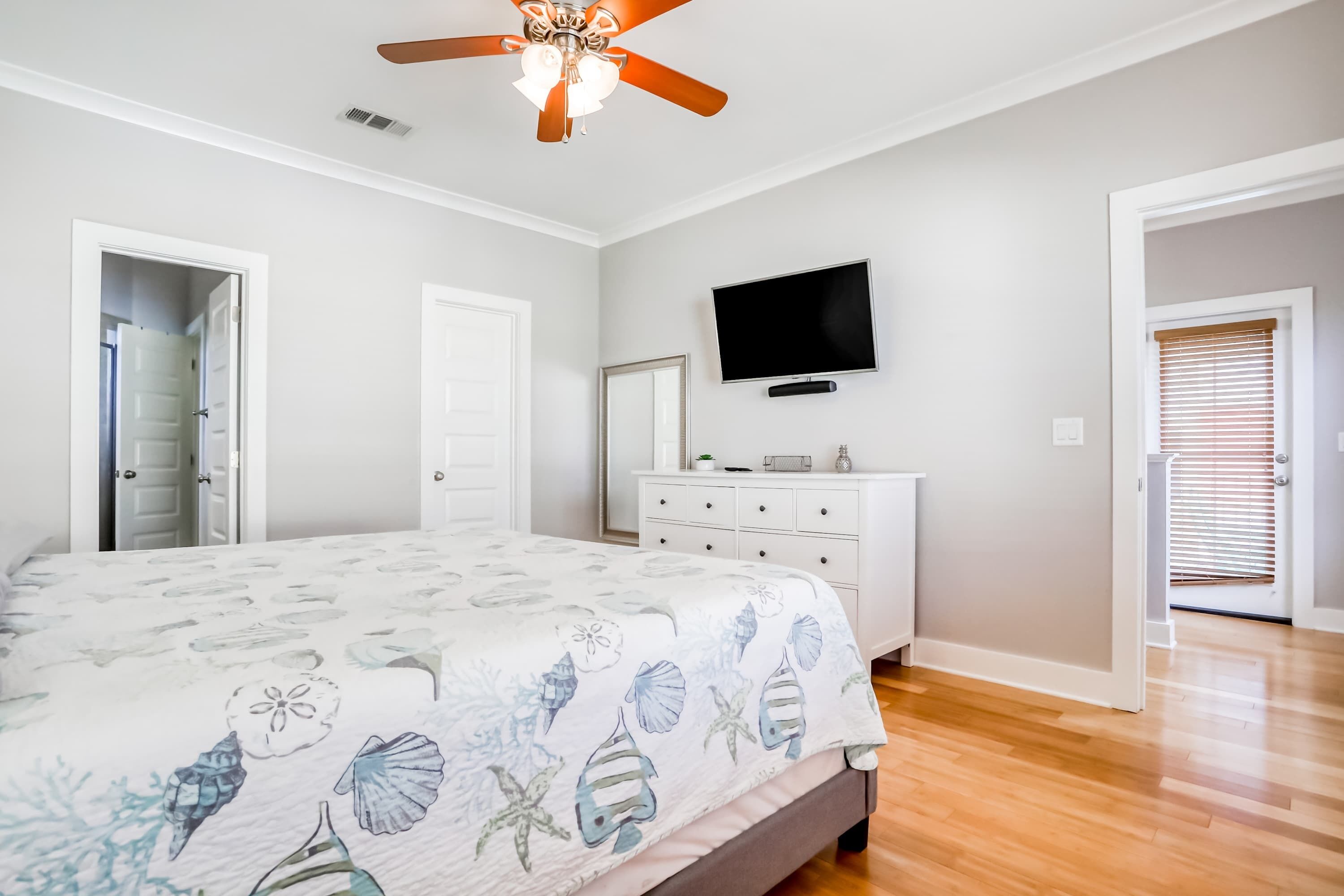 A bedroom with a bed, a ceiling fan, a TV, and a dresser.