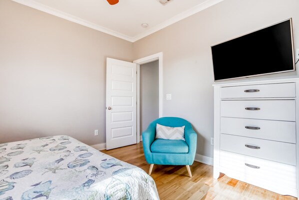 Ein Schlafzimmer mit einem Bett, einem blauen Sessel, einem Fernseher und einer weißen Kommode.