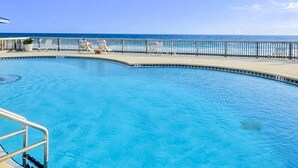 Una piscina con barandilla metálica, cielo azul despejado y vista al océano.