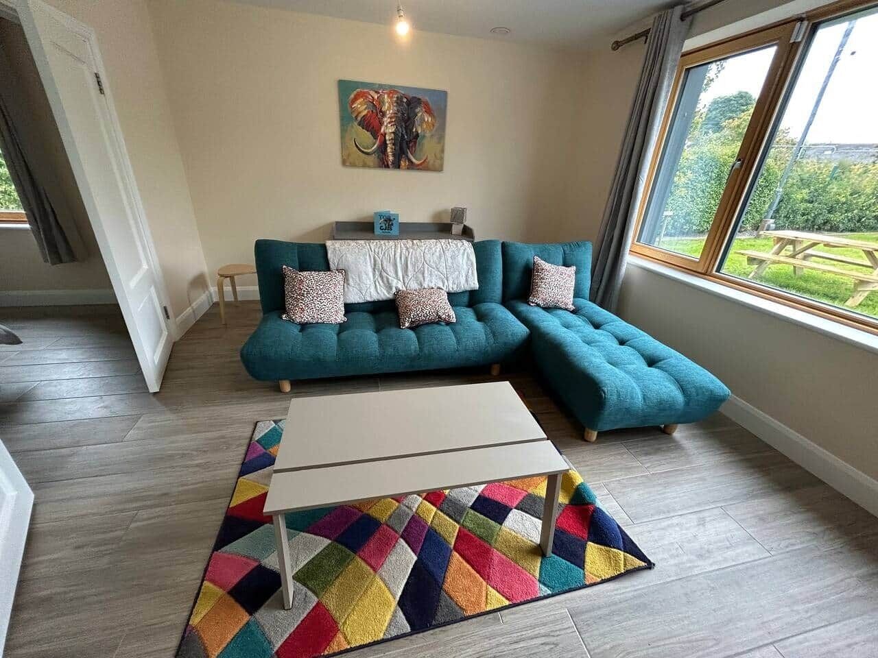 Ein modernes Wohnzimmer mit einem petrolfarbenen Modulsofa, einem weißen Couchtisch und einem farbenfrohen Teppich.