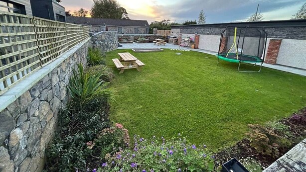 Ein Garten mit einer Steinmauer, einem Holzzaun, einem Rasen, einem Picknicktisch und einem Trampolin.