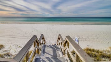 En trätrappa som leder ner till en strand med fri utsikt över havet.