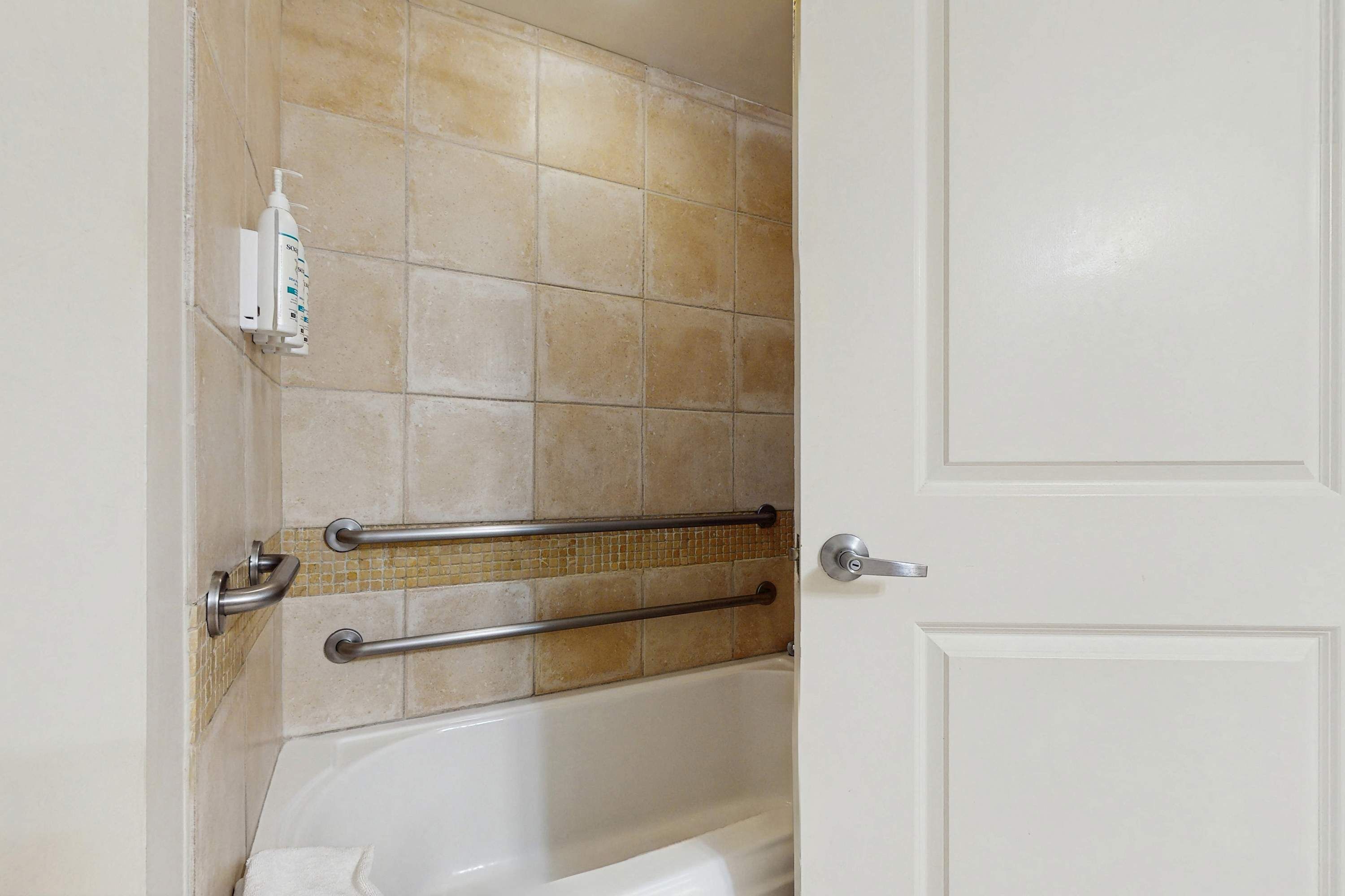A bathroom with a bathtub, grab bars, and a hand sanitizer dispenser.