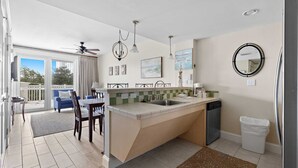 Eine moderne Küche mit einer großen Kochinsel, einem Essbereich mit blauem Sofa und Blick durch Glastüren.