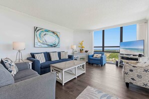 A modern living room with a sofa, coffee table, and TV. There is a large window with a view. - Waterfront getaway with ocean views, central AC & washer/dryer - walk to beach (Miramar Beach)