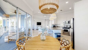 A modern kitchen with stainless steel appliances, a dining area with a wooden table and wicker chairs, and a large chandelier. - Lakefront condo with water-view balcony, private golf cart, resort pool & amenities (Miramar Beach)