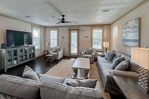 A spacious living room with a large flat-screen TV, comfortable seating, and a ceiling fan. - Gorgeous coastal home with pool, bikes, & large balcony - near beaches & parks (Santa Rosa Beach)