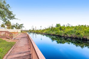 A wooden boardwalk along a calm river with greenery on one side and a building on the other. - Charming Condo at Waterside with Shared Pool, Hot Tub, Free WiFi, and AC (Mexico Beach)