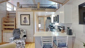 A compact kitchen with a central island, a dining area with two chairs, a staircase, and a framed picture on the wall. - Caney Creek | Great Views, Large Deck (Cosby)