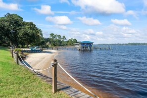 A wooden boardwalk leading to a dock with a blue-roofed structure, a sandy beach, and a calm lake with trees in the background. - Spacious townhome, dog-friendly w full kitchen & shared pool (Navarre)