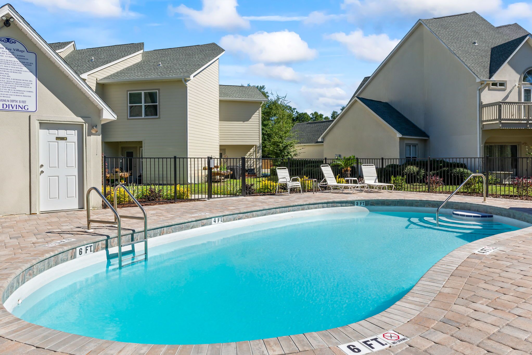 A swimming pool with a 6 ft depth sign, surrounded by a brick deck and lounge chairs.