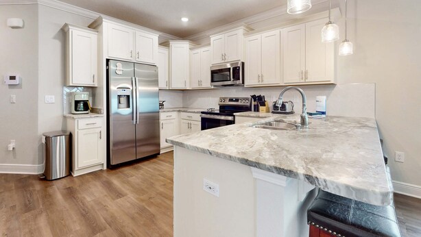 A modern kitchen with white cabinetry, stainless steel appliances, a marble countertop, and pendant lighting. - Spacious townhome, dog-friendly w full kitchen & shared pool (Navarre)