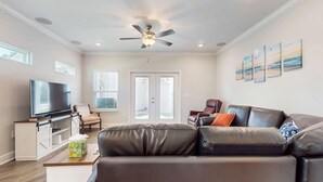 A modern living room with a flat-screen TV, leather sofa, ceiling fan, and artwork on the wall. - Spacious townhome, dog-friendly w full kitchen & shared pool (Navarre)