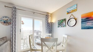 Un comedor con una mesa redonda y sillas blancas, un reloj en la pared y vistas a través de un ventanal.