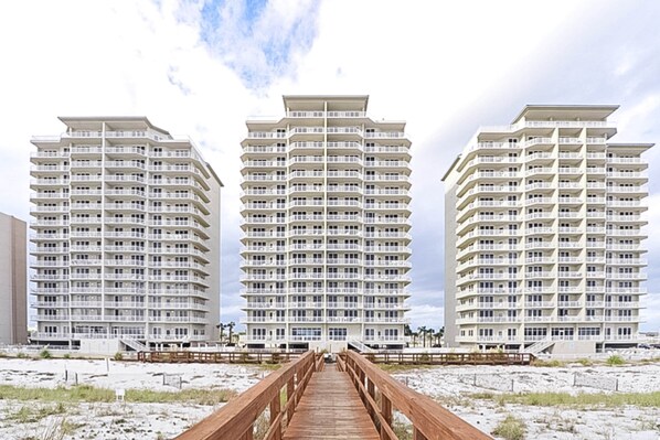 A beachfront hotel with a wooden boardwalk leading to three white buildings with balconies.