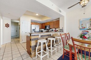 A modern kitchen with wooden cabinets, a central island with stools, and a dining area with a table and chairs.