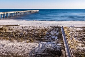 A beach with a wooden boardwalk leading to a pier extending into the ocean.